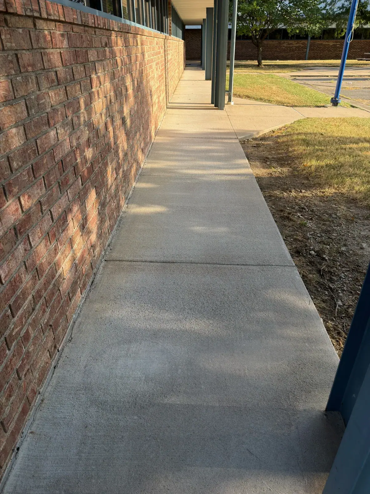 The cleaned walkway beside the same brick commercial building and blue columns